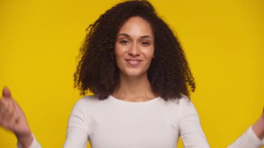 Mutlu genç bir kadın, yumruklarını sıkmış tezahürat yapıyor, parlak sarı arka planda neşeyle gülümsüyor.