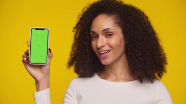 Yeşil ekran telefonu tutan neşeli bir kadın ve parlak sarı arka plan önünde 