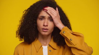 Stresli genç öğrenci endişeli ve bunalmış görünüyor, el alında, sarı arka planda izole edilmiş.