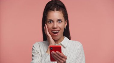 Şok olmuş, puantiyeli tişörtlü genç bir kadın akıllı telefonuna şaşkın bakıyor. Beklenmedik bir mesaja ya da alarma tepki veriyor..