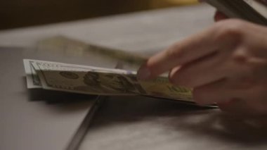 Kapalı bir dizüstü bilgisayarın yanında mermer bir yüzey üzerinde 100 banknotluk banknotları ayıran parmaklar nakit işleme veya finansmanı sembolize ediyor..