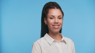 Yeşil ekran ile kameraya doğru akıllı telefon tutan gülümseyen genç bir kadın, mavi arka planda izole edilmiş, mobil uygulamaları veya UI modellemelerini göstermek için ideal.