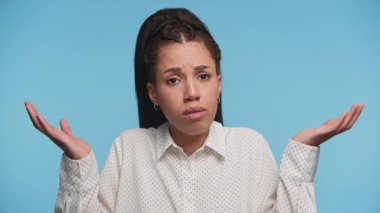 Şaşırmış genç bir kadın omuzlarını silkiyor ve ellerini kaldırıyor. Karışıklığı ifade ediyor ya da bilmiyor. Mavi bir arka plana kurulmuş..