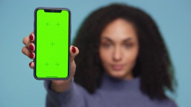Bir kadın tarafından tutulan yeşil ekranlı akıllı telefonun yakın plan görüntüsü, gösteriş uygulamaları, reklamlar veya mobil UI modellemeleri için ideal, mavi arkaplanda izole edilmiş..