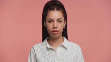 Beyaz benekli tişört giyen ciddi bir genç kadının portresi, tarafsız bir ifadeyle sade pembe bir zemine karşı duruyor..