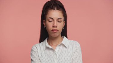 Ciddi bir yüz ifadesi olan genç bir kadın çenesini uzatmış, pembe bir arka planda derin düşüncelere dalmış..