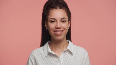 Genç bir kadın nazikçe gülümsüyor ve başını sallayarak onaylıyor ya da onaylıyor stüdyo ortamında pembe bir arka plana karşı duruyor..