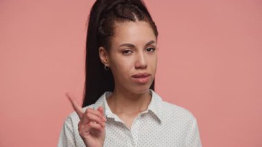Genç bir kadın parmağını kaldırmış, neşeli bir uyarı hareketi yapıyor. Pembe arka planda alaycı bir ifadeyle gülümsüyor..