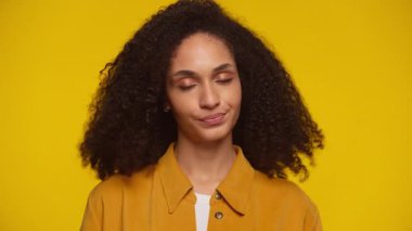 Gözleri kapalı ve tarafsız bir kadın. Onaylamadığını göstermek için başını nazikçe sallıyor. Parlak sarı bir arka plana karşı duruyor..