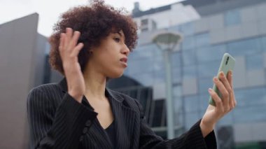 İş kadını, modern bir ofis binasının dışındaki bir video konuşmasında, hareketli el hareketleriyle kendini güvenle ifade ediyor..