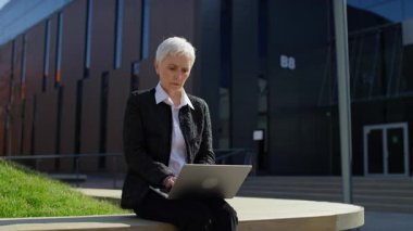 Dışarıda dizüstü bilgisayarla oturan yaşlı profesyonel kadın, hayal kırıklığı ve sonuçları gördükten sonra yüzünü hayal kırıklığı ya da strese sokuyor..