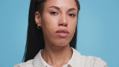 Ciddi bir ifadeyle kendine güvenen genç bir kadının portresi, sağlam bir mavi arkaplan karşısında duruyor, dayanıklılık ve kararlılık taşıyor..