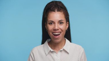 Şok olmuş genç bir kadın, ağzı ve gözleri açık, mavi bir arka plan karşısında duruyor, şaşkınlığını ve güçlü duygularını ifade ediyor..