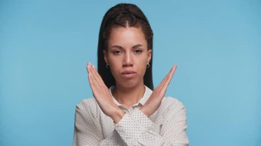 Kollarını göğsünün önünde birleştirerek dur ya da reddet diyen genç bir kadın ciddi bir ifadeyle mavi bir arkaplanda duruyor..