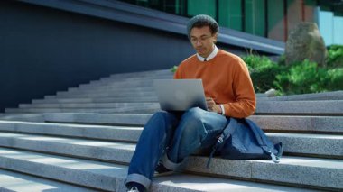 Şaşkın öğrenci şehir basamaklarında elleri ağızlarını kapatarak oturuyor, beklenmedik iyi haberlere duygusal tepki veriyor ve dizüstü bilgisayara bakıyor..