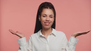 İki elini de kaldırarak gülümseyen neşeli genç bir kadın pembe arka planla iki farklı seçeneği dengeliyor ya da tartıyor gibi..