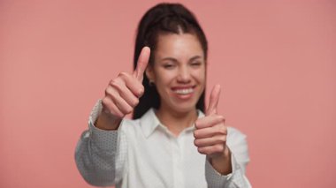 Büyük bir gülümseme ile iki baş parmak gösteren mutlu genç bir kadın, pembe bir arka plana karşı onay, memnuniyet ya da teşvik ifade.