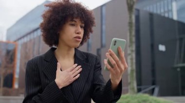 Takım elbiseli genç bir kadın, modern bir kentsel alanda, akıllı telefon görüntüleriyle duygusal bir konuşma yapıyor..