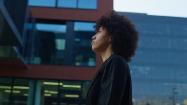 Takım elbiseli profesyonel bir kadının kasıtlı olarak şehir merkezindeki modern bir ofis binasına doğru yürüyüşünün yan görüntüsü..