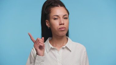 Ciddi bir kadının işaret parmağıyla uyarı jesti yaptığı portresi. Stüdyonun mavi arka planına karşı..