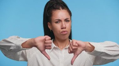 Hoşnut olmayan genç bir kadın, mavi bir arka plana karşı ciddi bir yüzle iki kez baş aşağı hareket ediyor. Onaylamadığını gösteriyor..