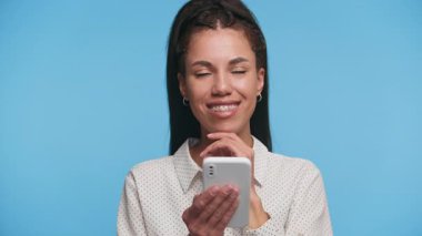 Akıllı telefon tutan ve düşünceli bir şekilde gülümseyen genç bir kadın. Potansiyel online alışverişi tatmin edici bir ifadeyle düşünüyor..