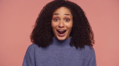 Heyecanlı, ağzı açık ve anlamlı gözleri olan genç bir kadın pembe bir arka plana karşı inanılmaz olumlu haberlere sevinçle tepki veriyor..