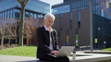 Modern bir ofisin dışında çalışırken bir çözüm bulduktan sonra gülümseyen ve dizüstü bilgisayarına işaret eden kendinden emin yaşlı kadın..