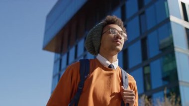 Turuncu eşofman altı ve bereli şehir gençliği modern şehir bölgesinde güvenle yürüyor, hırs ve kişisel tarzını gösteriyor..