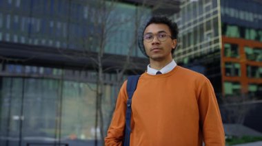 Günümüz akademik binasının önünde gözlüklü ve sırt çantalı genç bir erkek öğrenci, ciddi bir şekilde ileriye bakıyor..