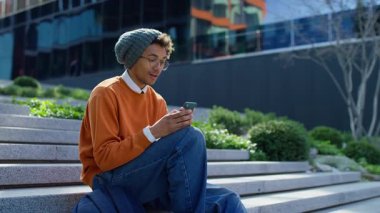 Genç adam, akıllı telefonuyla bir mesaj okuyup sınav başarısını veya kampüs basamaklarında spor zaferini kutlarken sevinçle tepki veriyor..