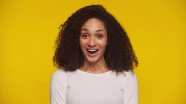 Neşeli genç bir kadın gülümseyip yumruğunu sallıyor. Zaferini ve motivasyonunu canlı sarı bir arka plana karşı gösteriyor..