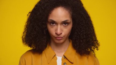 Kızgın kadın doğrudan kameraya bakıyor sarı arka planda sert ve yoğun bir ifadeyle, odaklanmayı, meydan okumayı veya kararlılığı iletiyor.