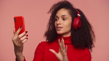 Videodaki kadın pembe arka planda kırmızı kulaklık takıyor.