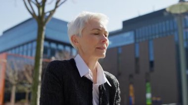 Yaşlı iş kadını dışarıda, laptopunu kullanırken düşünceli bir ifadeyle duruyor, önemli bir iş kararını değerlendiriyor..