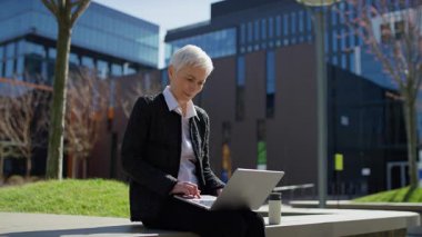 Olgun bir kadın şehir dışında oturmuş güneşli bir günün tadını çıkarırken internetten içeriğine bakıyor..