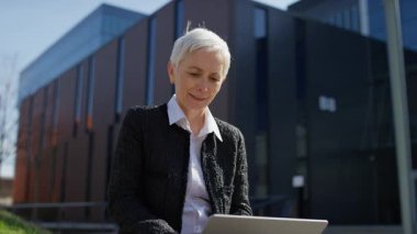 Dışarıda dizüstü bilgisayarıyla oturan mutlu yaşlı kadın, olumlu haberler okurken neşeli bir sürpriz yapıyor ya da internetten heyecanlı bir mesaj okuyor..