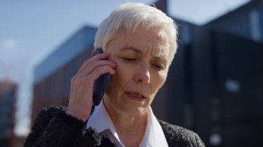 Neşeli, olgun bir kadın dışarıda güzel bir telefon görüşmesi yapıyor. Günışığında modern bir ofis binasının yanında duruyor..