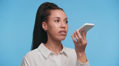 Genç bir kadın akıllı telefonunu tutuyor ve ona doğru konuşuyor. Ses asistanı kullanıyor gibi görünüyor, bir mesaj kaydediyor ya da sesli arama yapıyor..