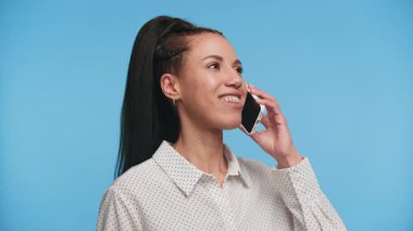 Önünde akıllı telefonunu tutan odaklanmış genç bir kadın açık mavi bir arkaplan karşısında hoparlörden konuşuyor..