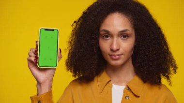 Kendine güvenen bir kadın, yeşil ekranlı akıllı telefonu sarı arka planda gösteriyor. Mobil uygulama promosyonu için mükemmel..