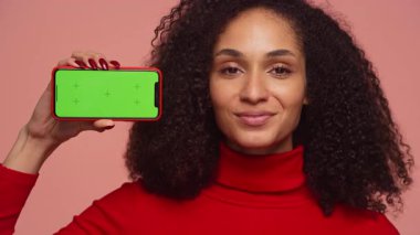 Mutlu bayan müşteri yeşil ekranlı akıllı telefonu tutarken onaylıyor, pembe arka plana karşı memnuniyetini ifade ediyor.