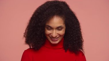 Kıvırcık saçlı, kendine güvenen, onaylı, gülümseyen pembe arka planda onay ve pozitiflik gösteren kendine güvenen genç bir kadın..