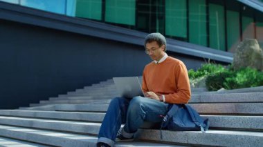 Genç adam dışarıda merdivenlerde oturuyor, heyecan içinde sevinçten havalara uçuyor dizüstü bilgisayardan olumlu haberler okuyor, muhtemelen sınavı geçiyor..