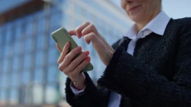 Modern cam bir binanın önünde dikilirken son sınıf öğrencisi kadınların akıllı telefonlarıyla daktilo çektikleri yakın çekim..