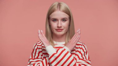 Çizgili tişörtlü sarışın bir kadın X işaretinde kollarını tutuyor. Pembe arka planda reddedilme ya da yasaklama sinyalleri veriyor..