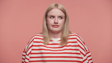 Kırmızı çizgili tişörtlü sarışın kadın pembe bir arka plana karşı kafa karışıklığı ya da tereddüt göstererek omuz silkip şüpheli bir yüz ifadesi takınıyor..