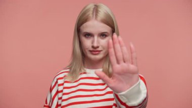 Kırmızı çizgili tişörtlü sarışın kadın kameraya el kaldırıyor, işaret veriyor ya da pembe arka planı reddediyor..