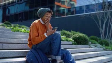 Dışarıdaki merdivenlerde oturan genç öğrenci, akıllı telefona bakarken ağzı açık kalmış, şok edici ya da şaşırtıcı haberlere tepki veriyor..