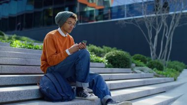 Basamaklarda oturan, ağzı açık ve eli yüzü açık akıllı bir öğrenci dışarıdaki şaşırtıcı ve olumlu haberlere tepki veriyor..